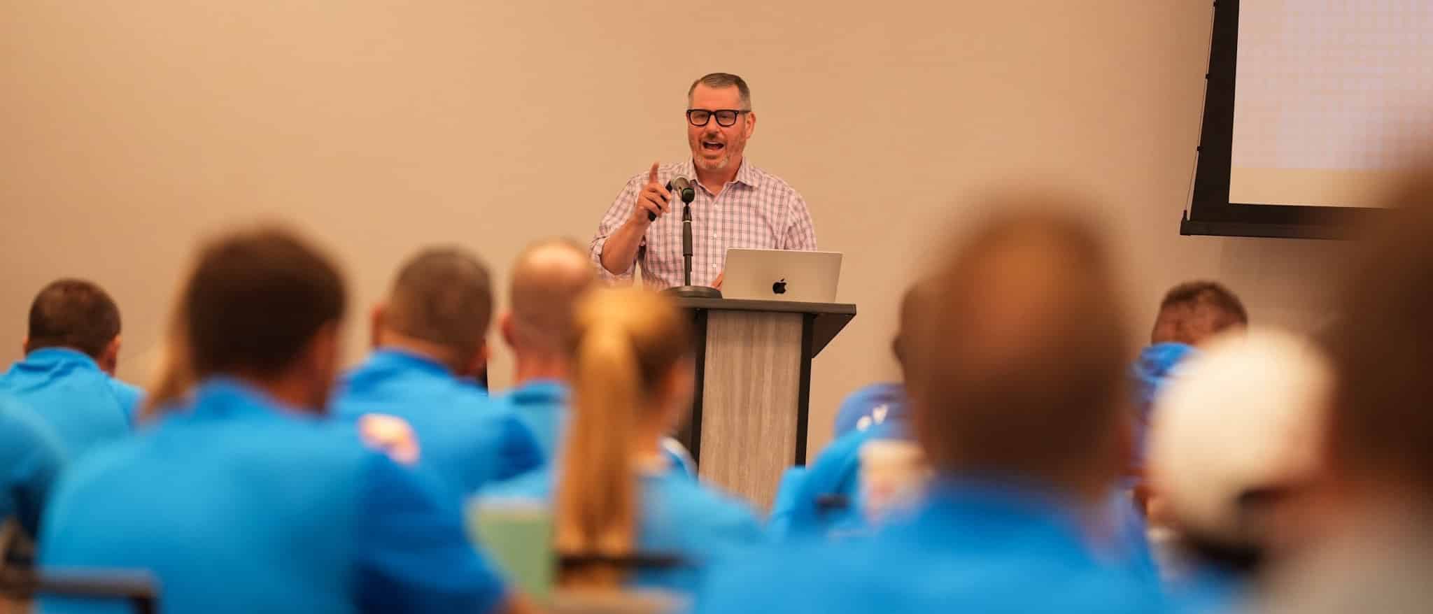 Jerry Macnamara delivering the keynote at the JFC Coaches Symposium, speaking from the podium to a room of coaches