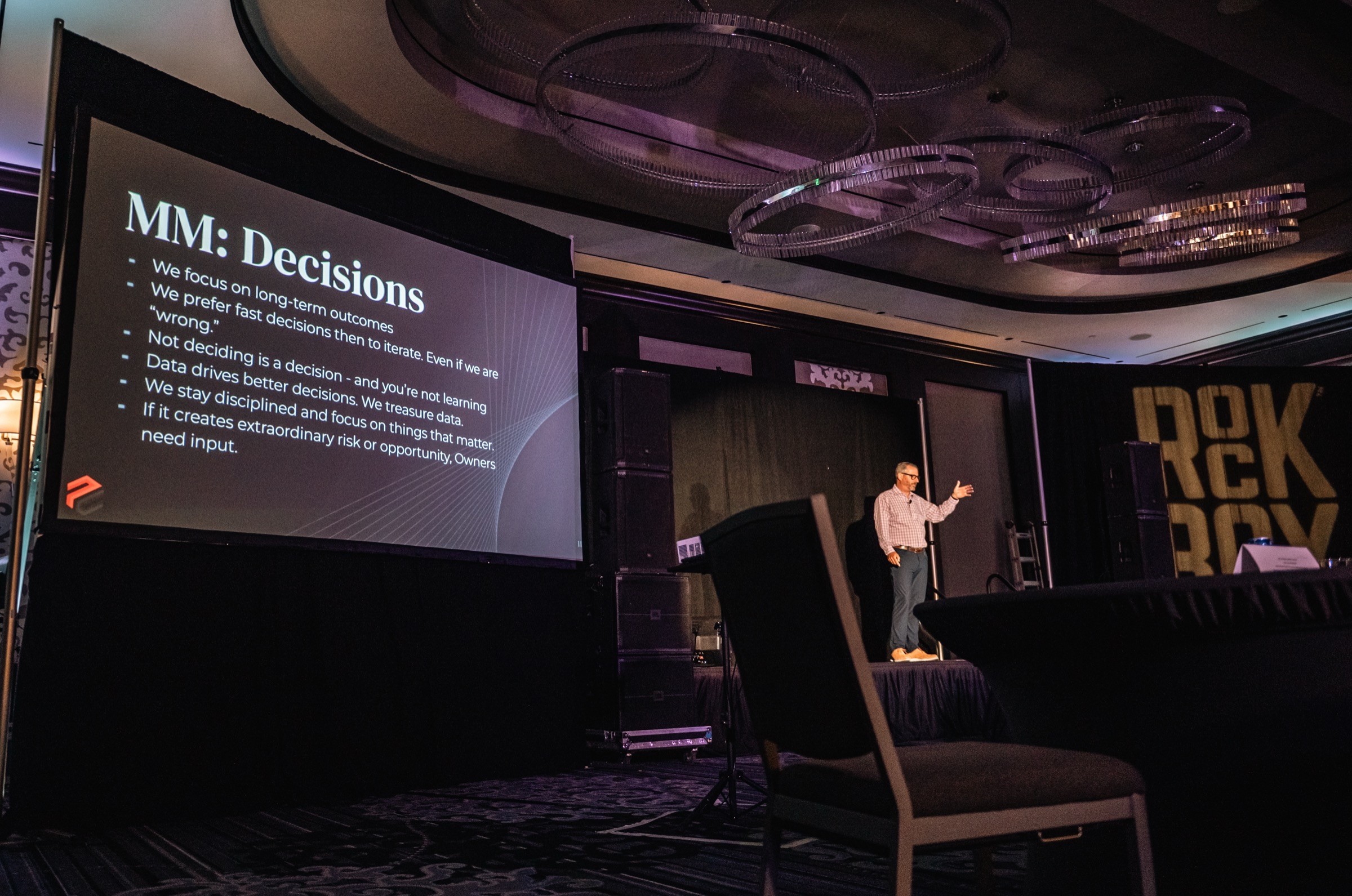 Jerry Macnamara on a main stage beside a large screen showing the MM: Decisions framework