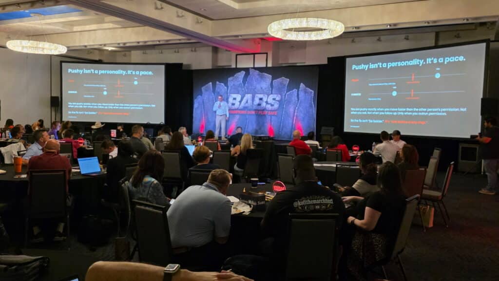 The main-stage room at the Badass Business Summit 2026 in Dallas, about 200 attendees, with Jerry Macnamara on stage between two screens